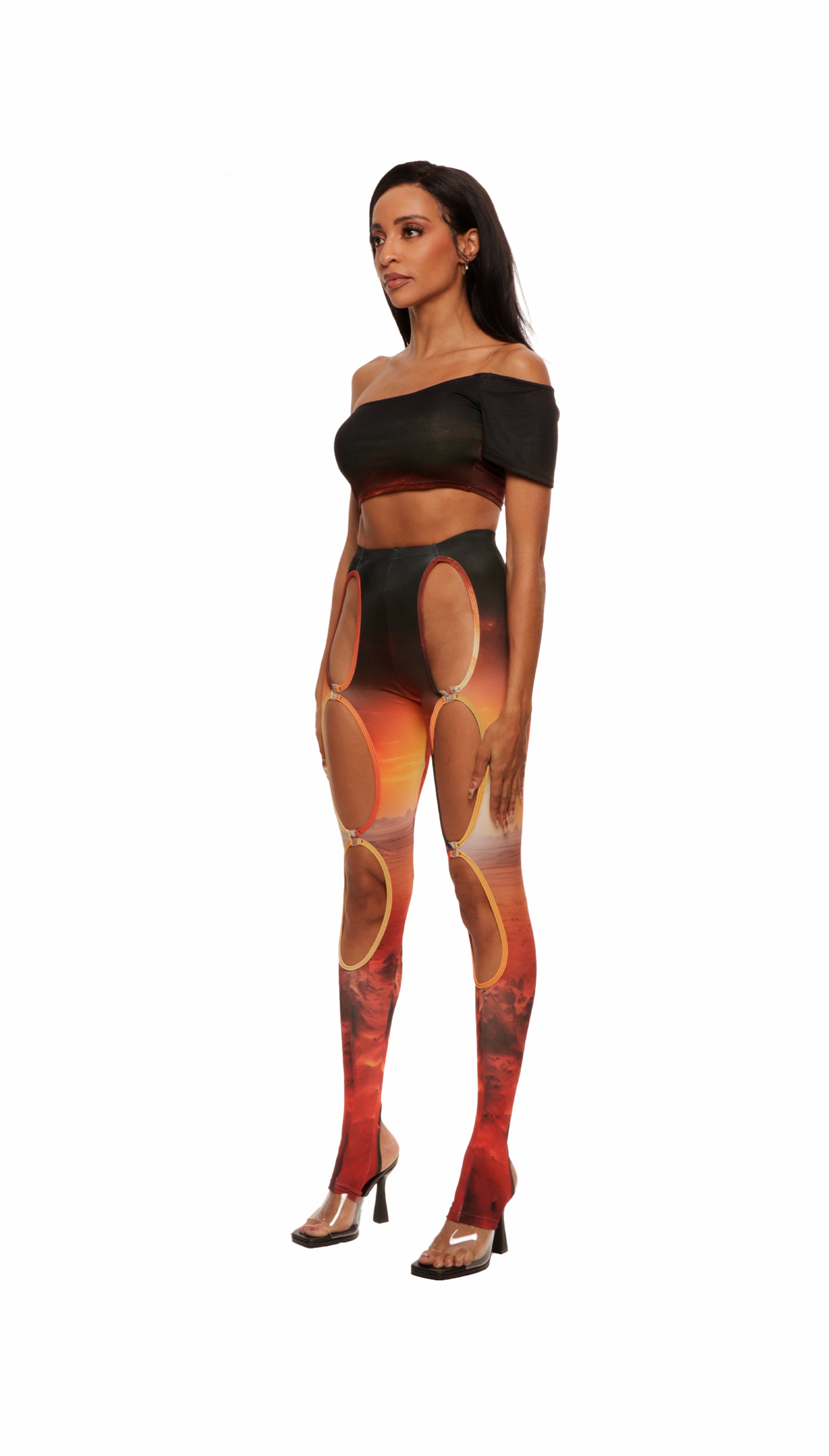 Angle view of woman who looks like Beyonce or Aaliyah wears sunset printed jersey leggings with cutout details in the front attached with snaps and heel cutout